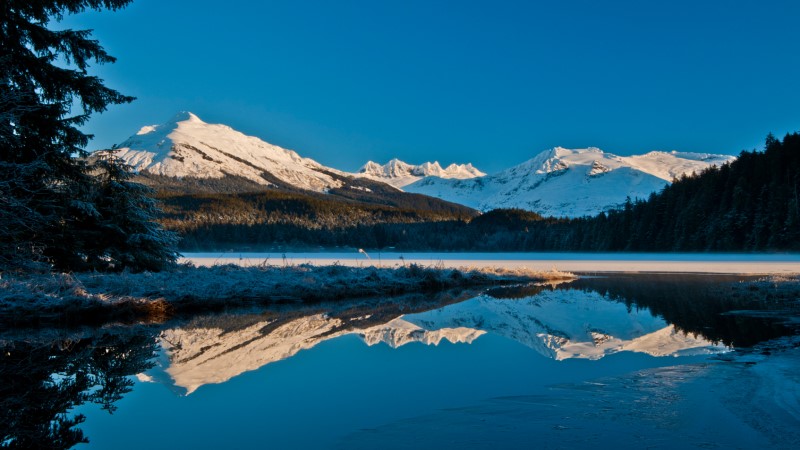 Vista panorâmica das geleiras de Juneau, no Alasca, com um espelho de água refletindo as montanhas com picos nevados