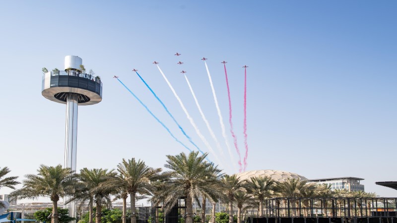 Garden In The Sky, torre com 250 metros na Expo 2020 Dubai, com terraço panorâmico 360 graus, tendo ao fundo um céu azul que é percorrido por uma esquadrilha de nove aviões que emitem faixas de fumaça nas cores azul, branco e vermelha.