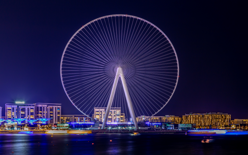 Vista noturna da roda-gigante The Ain, em Dubai, tendo ao fundo prédios iluminados.