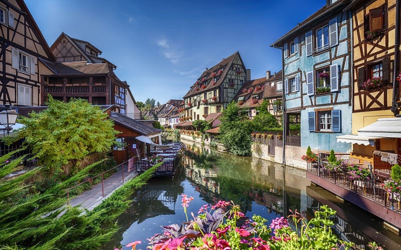 cruzeiros fluviais: Canal na cidade de Estrasburgo, na França, com casarios coloridos típicos, com janelas de madeira e jardineiras com flores.