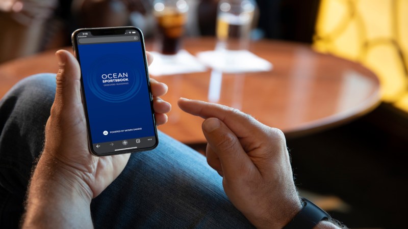 Homem segurando celular com as duas mãos, visualizando aplicativo Ocean Medallion.