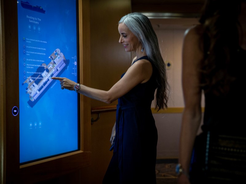 Mulher parada em frente a uma tela vertical interage com o mapa do navio.