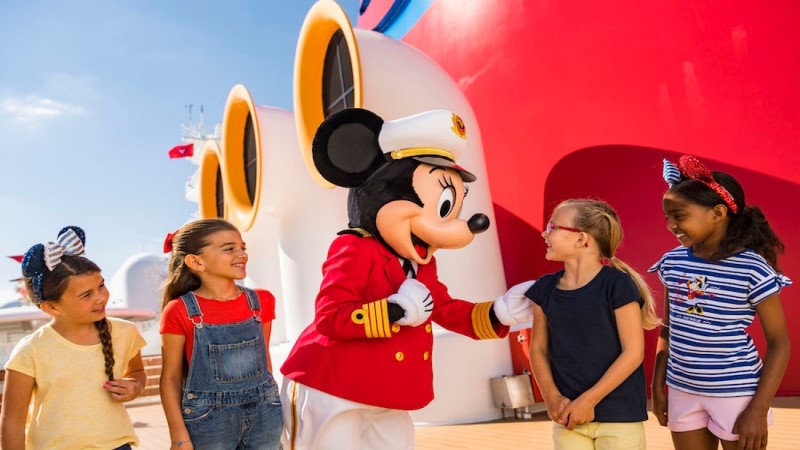 A personagem Minnie Mouse interage com quatro meninas, no deck de um navio da Disney.