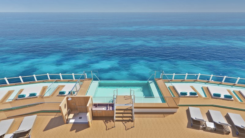 Vista aérea de piscina com borda infinita e cadeiras de sol, no deck do navio, tendo mar azul ao fundo.