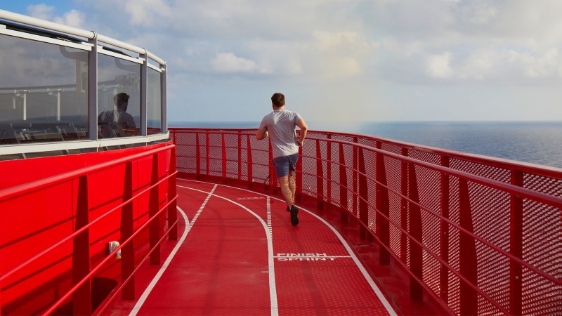 Pista de corrida no deck do Scarlet Lady, novo navio da Virgin Voyages; circuito pintado de vermelha, com guarda-corpo vermelho nas duas laterais, tendo ao fundo o horizonte do mar e céu azul.