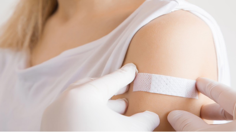 protocolos de segurança: Mãos com luvas brancas colocam um curativo sobre o braço de uma mulher, após vacinação.
