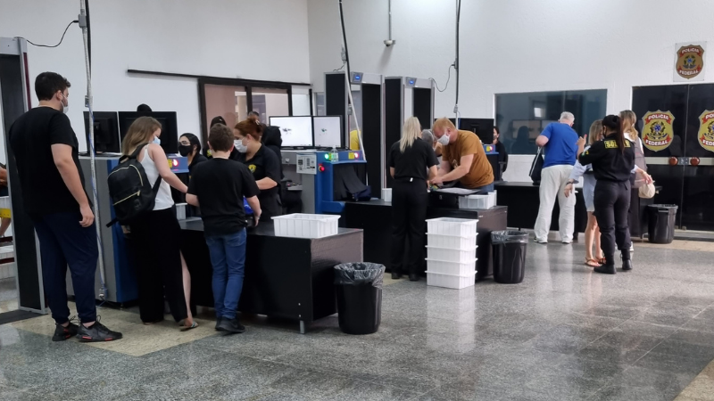 Área de raio-x no embarque do Porto de Santos, com viajantes colocando bagagem nas esteiras para leitura de raio-x