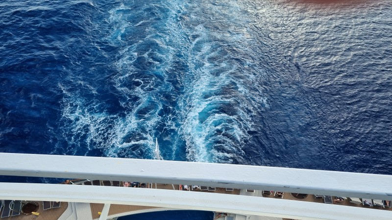 Vista aérea da popa do navio, com rastro dos motores do navio MSC Seaside, na água azul do mar.