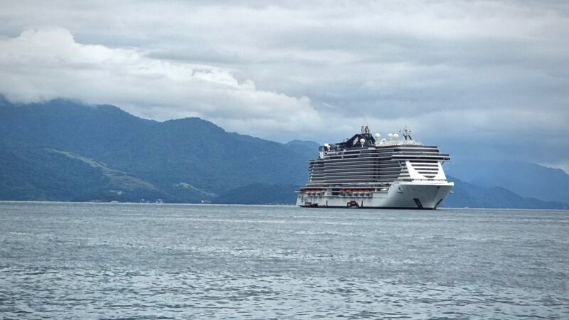 Paisagem com navio MSC Seaside ao longe, mar em primeiro plano e, ao fundo, cadeia de montanhas da Ilha Grande, no Rio de Janeiro.