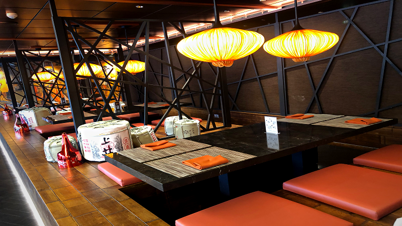 Ambiente do restaurante japonês Pan Asian, com mesas baixas e almofadas vermelhas para os clientes sentarem; sobre a mesa, lanternas japonesas amarelas.