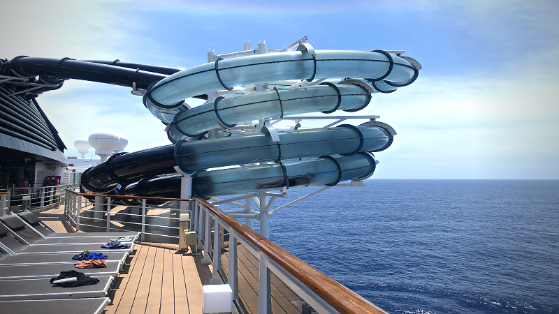 Tobogã de água na lateral do navio MSC Seaside, com tubos transparentes avançando para fora da lateral do navio, sobre o mar.