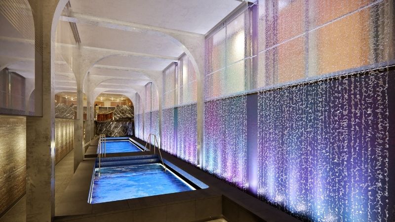 Área termal do novo spa NCL, o Mandara Spa, com piscinas e cascata de águas caindo sobre a parede lateral